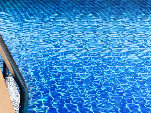 Close-up of clear blue pool water with metal handrail.