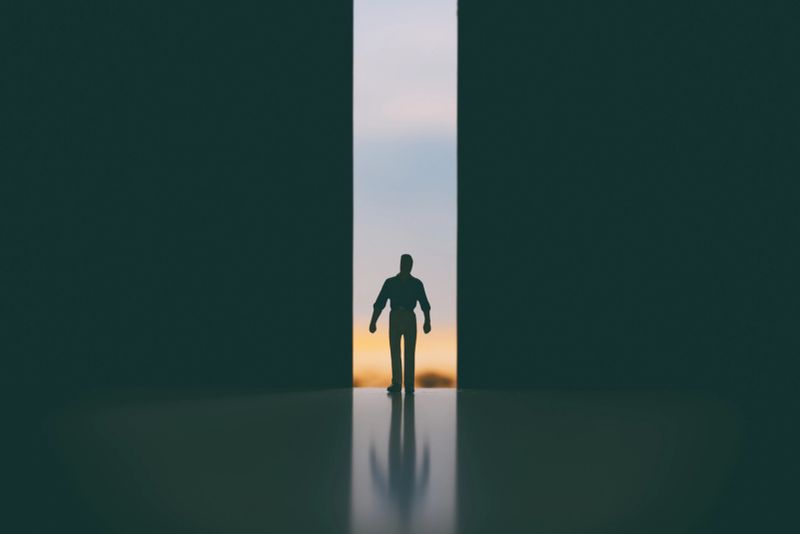 A man walks through a doorway from a bright desert location into a vast dark space (miniature photography).