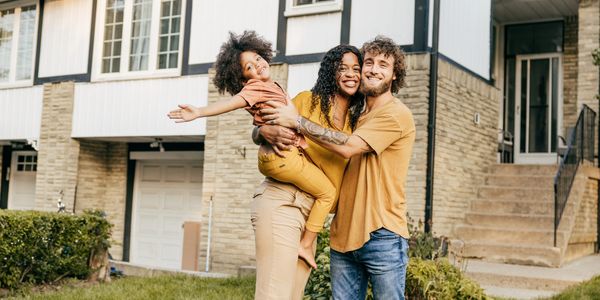 Happy family of three posing and smiling outside their home.