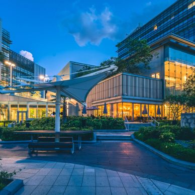 Modern building complex illuminated at dusk with outdoor seating.