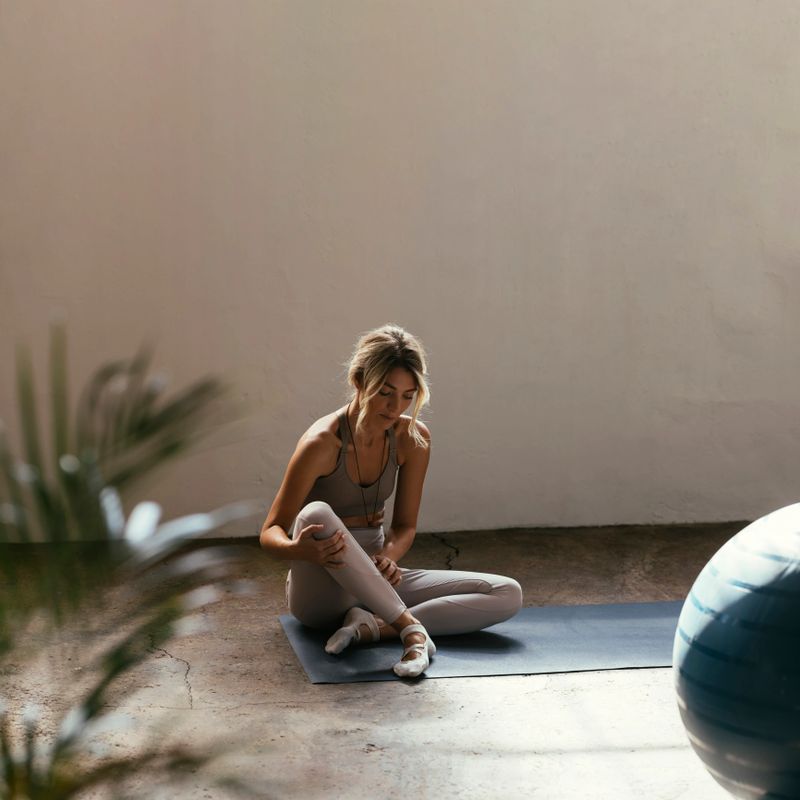 A horizontal portrait of a young Caucasian woman doing yoga on a mat indoors sitting looking away