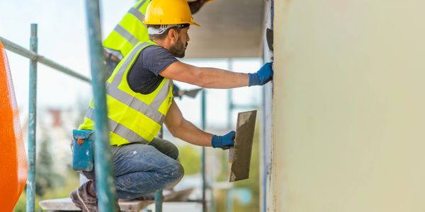 Construction worker smoothing wall plaster on scaffolding.