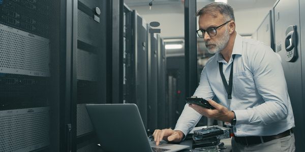 IT professional troubleshooting servers in a data center with a laptop.