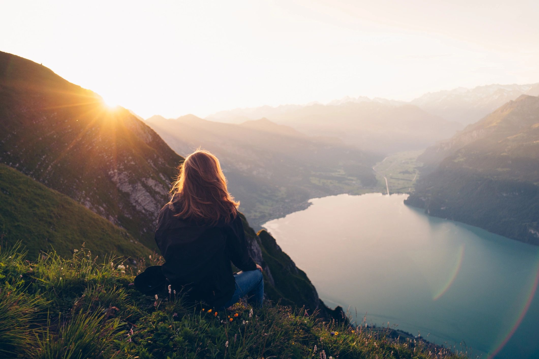 Person watching sunrise over mountains and lake.