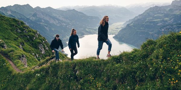 Three hikers walking along a mountain path above a lake, symbolizing journey and forward movement. I