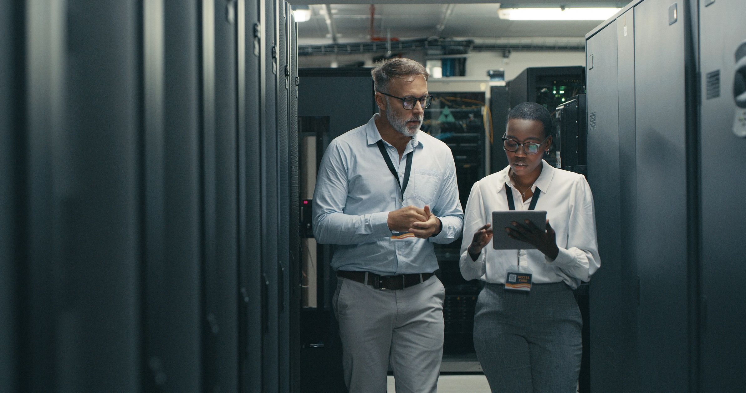 Two IT professionals discussing data in a server room using a tablet.