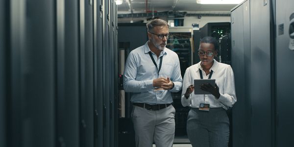 Two IT professionals discussing data on a tablet in a server room.