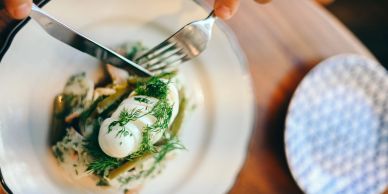 Fork and knife cutting into a dill-covered dish.