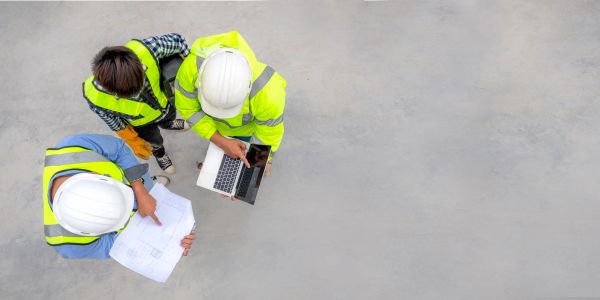 Three construction workers reviewing plans and laptop.