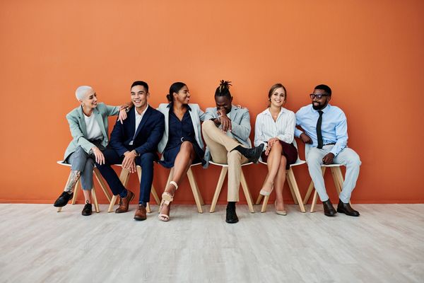 Diverse group of professionals sitting and smiling against an orange wall.