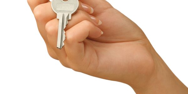 Hand holding a silver house key against a white background.
