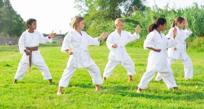 Multinational group of schoolchildren, boys and girls, practicing karate at the park outdoors
