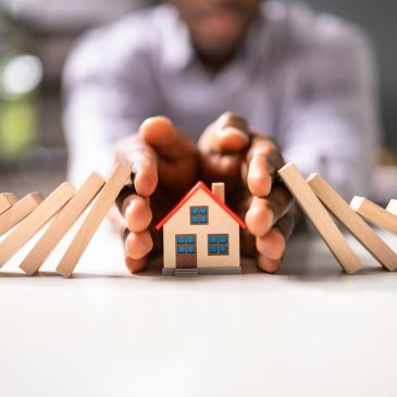 Hands protecting a small house from falling dominoes.