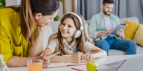 Mother helping daughter with homework while father uses tablet.