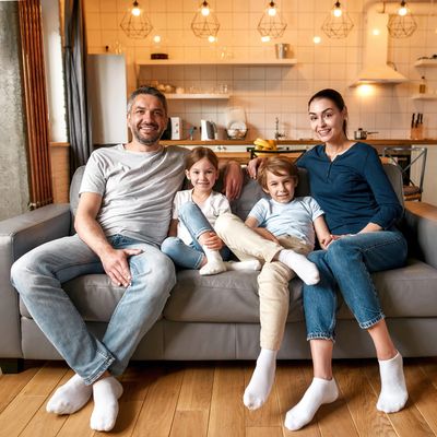 Happy family of four sitting together on a gray couch in a cozy living room.