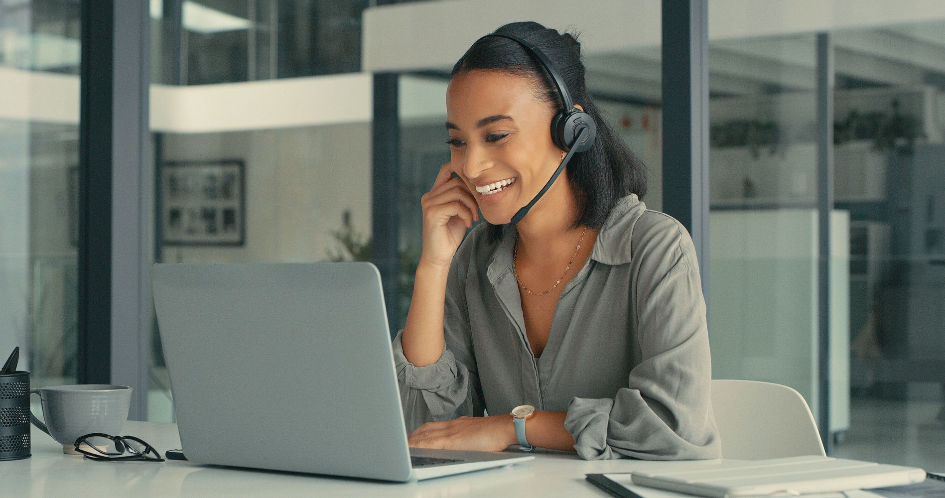 Smiling woman wearing headset working on laptop in modern office.
