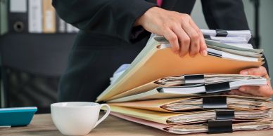 Person organizing a stack of folders on a desk.