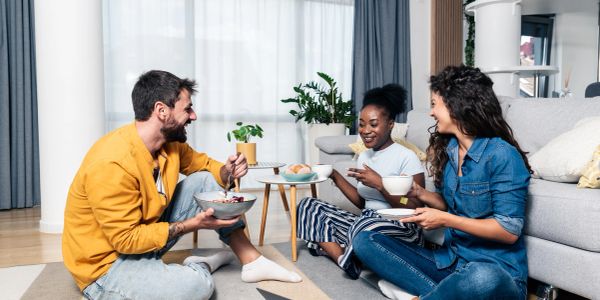 Three friends eating and chatting on the floor.