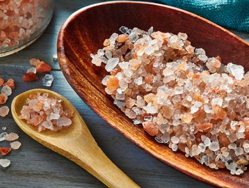Coarse Himalayan pink salt crystals in a wooden spoon and bowl.