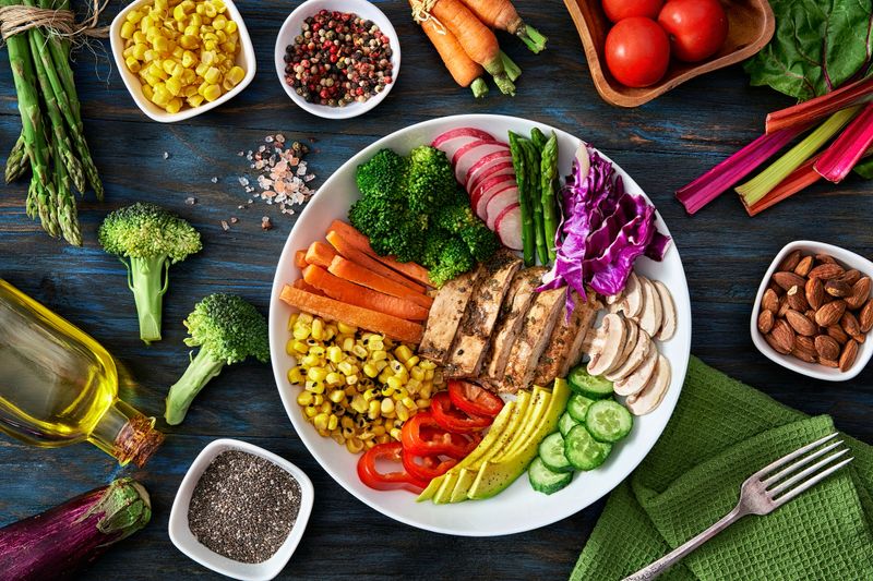 Healthy eating and diet concepts. Colorful spring salad on rustic white wood table. Included ingredients: Chicken, tomatoes, broccoli, lettuce, bell peppers, mushroom, carrots, radicchio, almonds.