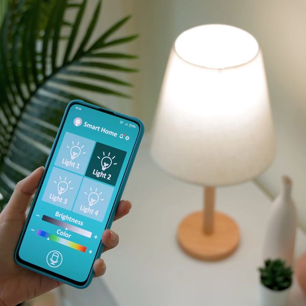Person controlling smart home lights using a mobile app near a table lamp.