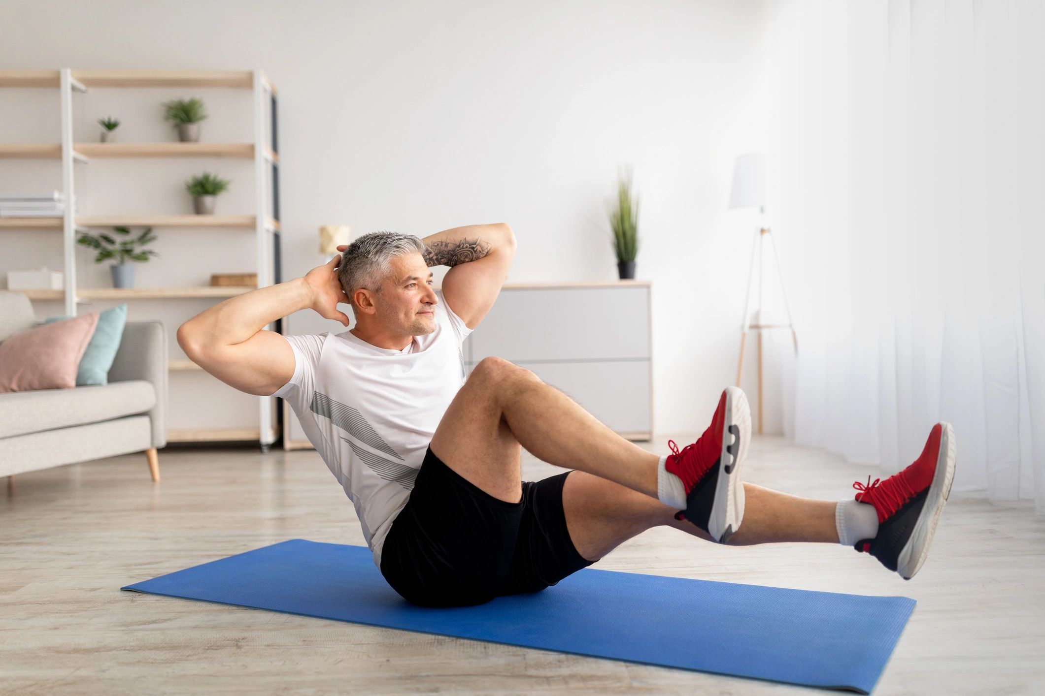 Man exercising on a blue mat in a bright, modern living room.