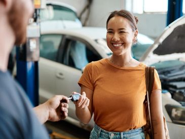 A woman happily receives car keys from a mechanic in a repair shop.