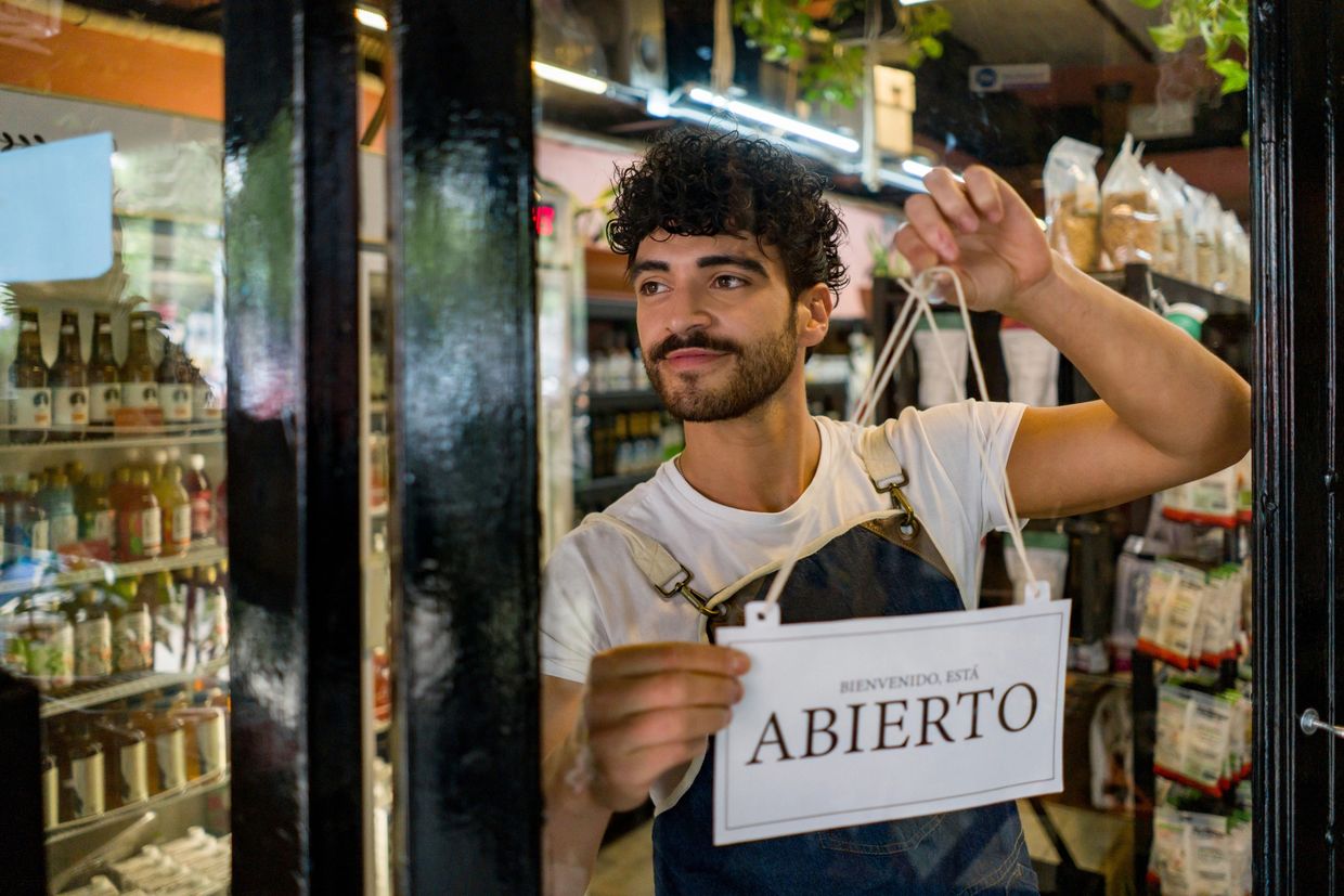 Man hanging an "Abierto" (Open) sign on a store door.