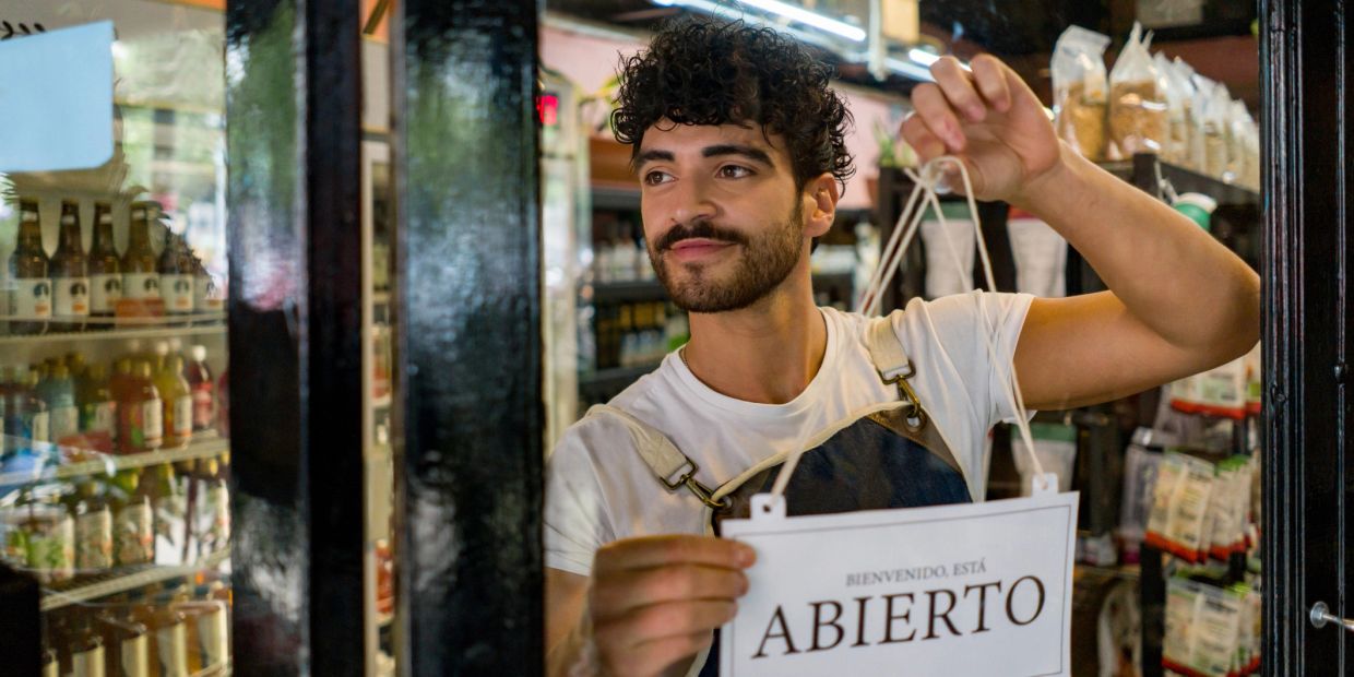 Man hanging an "Abierto" (Open) sign on a store door.