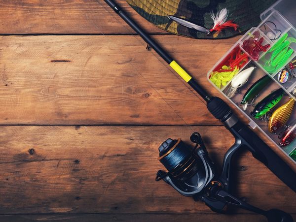 Fishing rod and tackle box filled with lures on a wooden table.