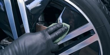 Person wearing black gloves cleaning a shiny car wheel with a green cloth.