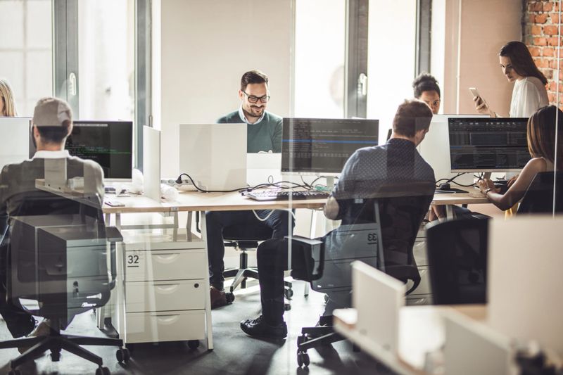 Large group of computer programmers working in the office. The view is through glass.