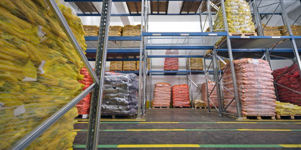 Warehouse storage with pallets of bagged produce organized on metal racks.