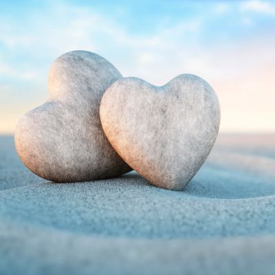 Two heart-shaped stones resting on a sandy surface under a soft sky.