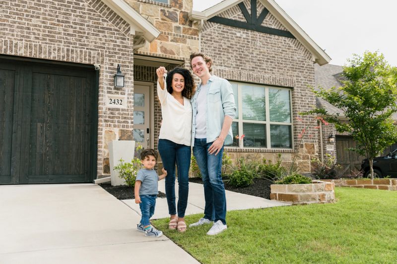 The young family stands in the  front yard and proudly displays the keys to their new home.