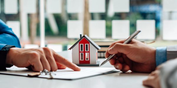 Two people discussing a contract with a small house model on the table.
