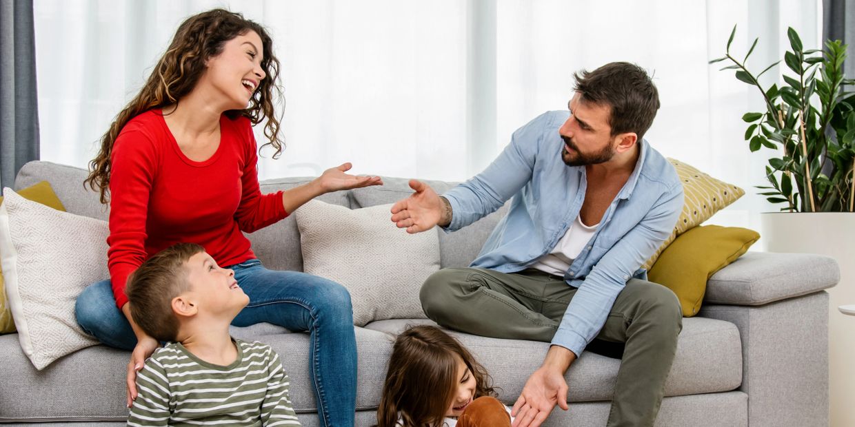 A happy family of four talking and laughing together on a couch.