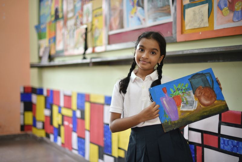 Portrait of a school girl holding her still life painting  in Art room