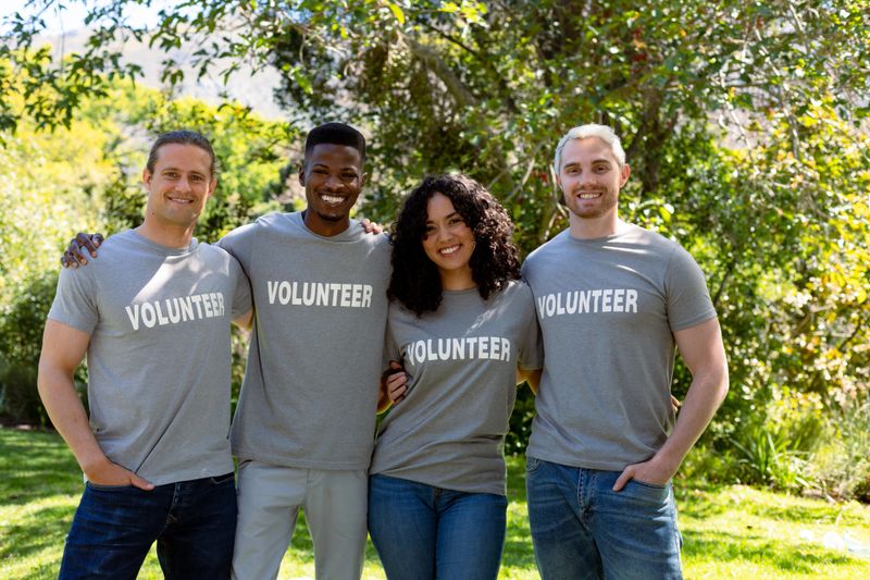 Group of smiling deverse female and male volunteers in matching tshirts looking at camera. eco conservation volunteers doing countryside clean-up.