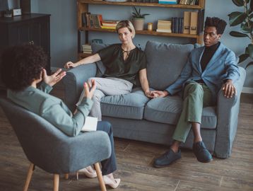 Couple holds hands while talking with therapist.