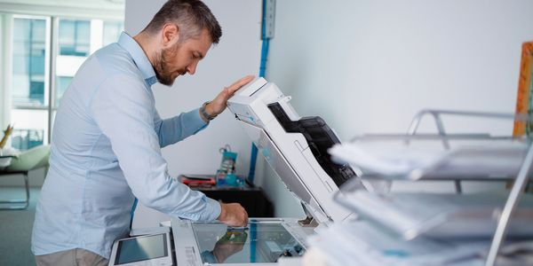 Man clearing a paper jam in a photocopier inside an office.