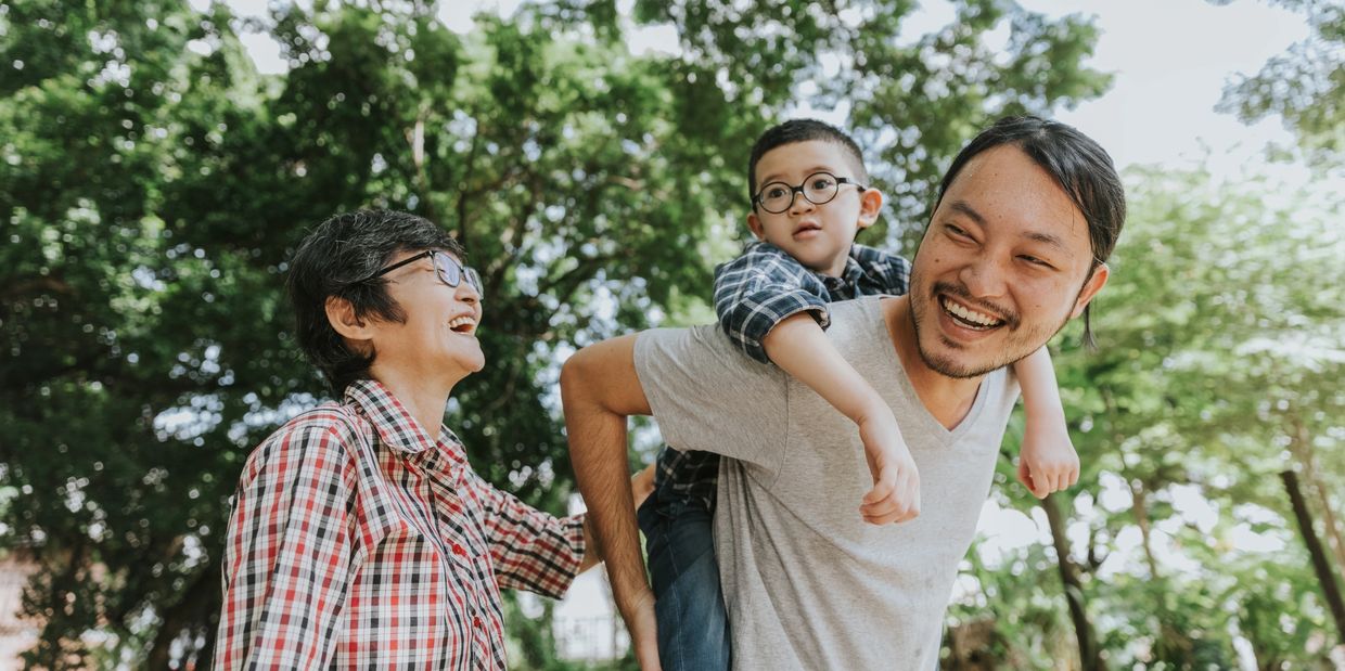 A joyful family enjoying a sunny day outdoors with a child on dad's back.