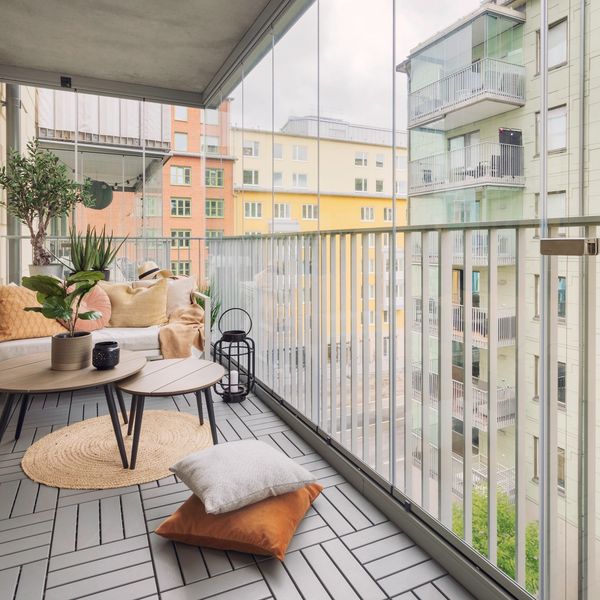 Cozy balcony with modern furniture and glass railing overlooking city buildings.