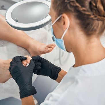 A professional wearing black gloves performs a foot care treatment on a client.