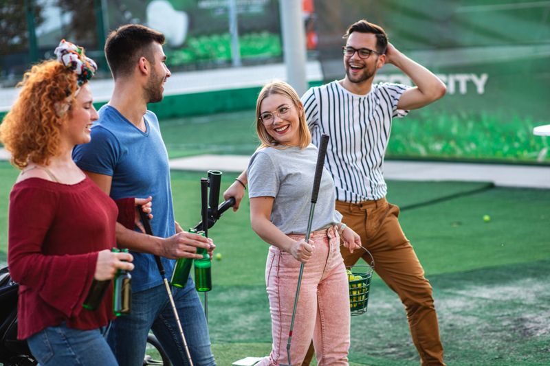 Group of smiling friends enjoying together playing mini golf in the city.
