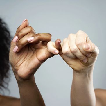 Two hands of different skin tones linking pinky fingers in a gesture of promise.