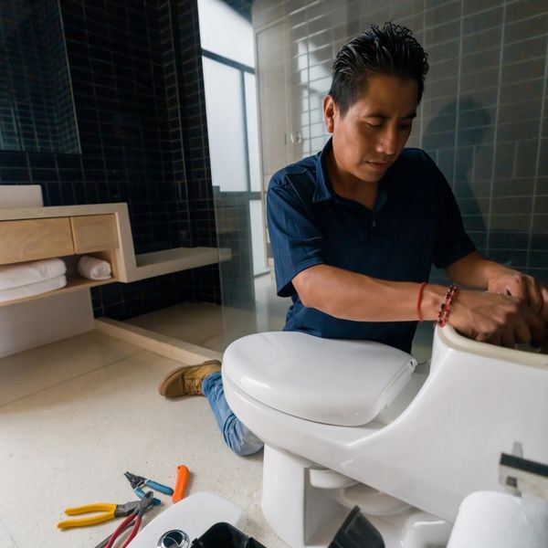 A plumber repairing a white toilet in a modern bathroom.