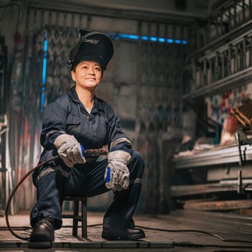 A female welder in protective gear sitting confidently in a workshop.