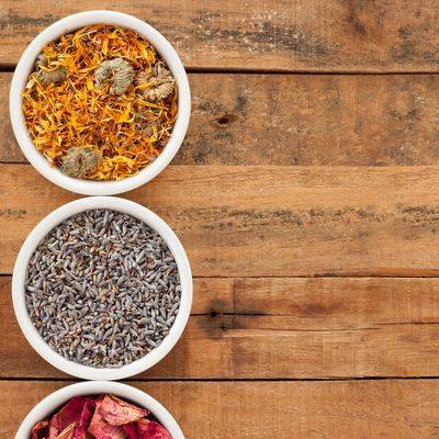 Three bowls with dried flowers and herbs on a wooden surface.