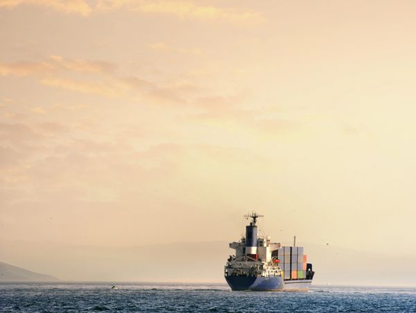 A cargo ship sails on calm waters during a golden sunset.